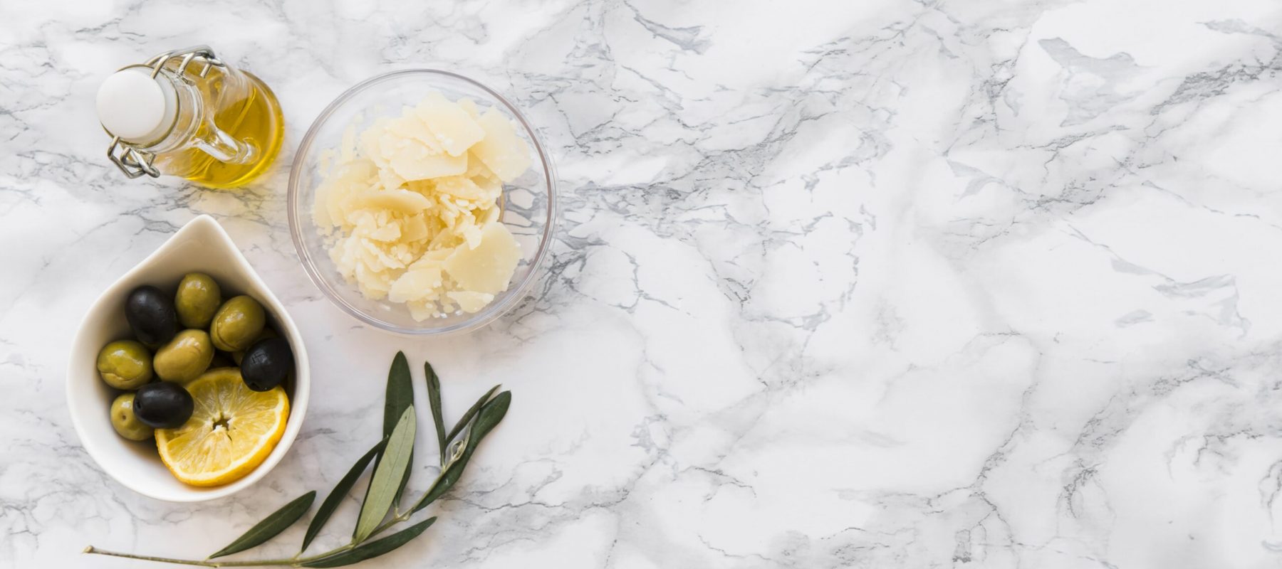 grated-cheese-with-olive-lemon-slice-bowl-oil-bottle-white-backdrop-min